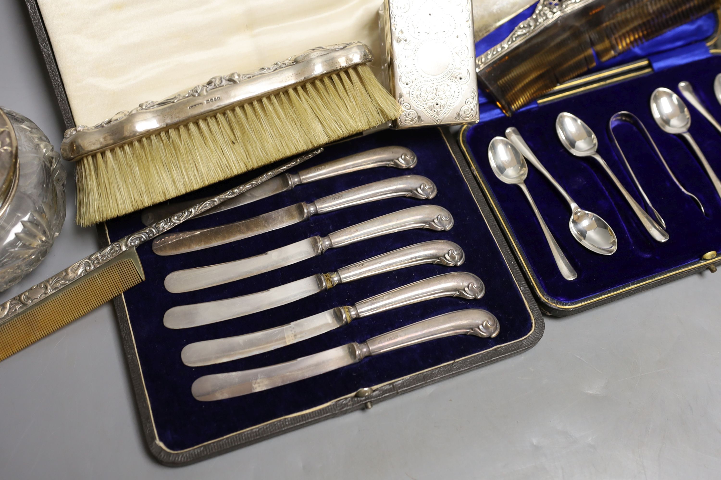 Four assorted silver mounted glass toilet jars, a silver mounted brush, two combs and a shoe horn and two cased sets of cutlery including silver teaspoons with tongs.